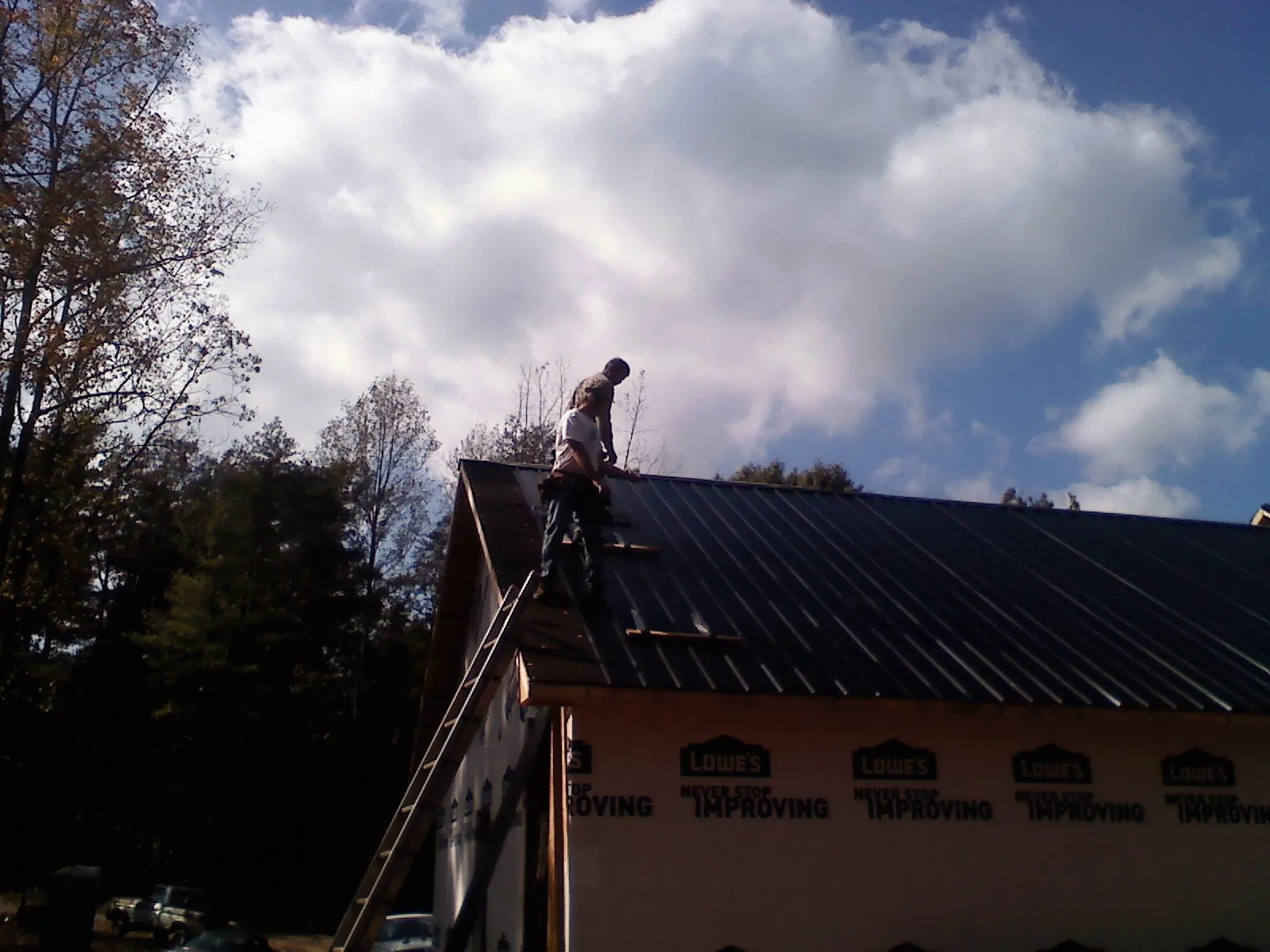 Roofer fastening dark metal panels high against a cloudy sky, from a Roof Inspection job in Lisle