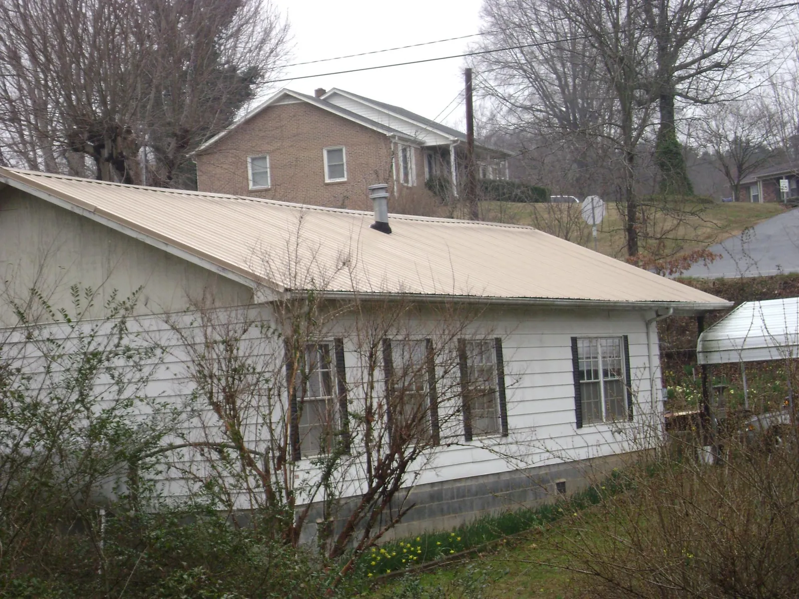 Tan metal roof on a white sided house set into a hillside — Commercial Roofing by Roofing Brothers in Lisle